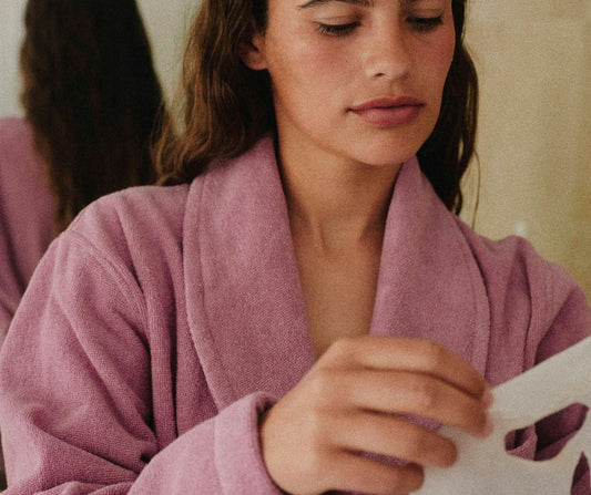 Woman in pink bathrobe with a face mask in hand