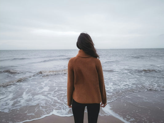 Woman in sweater on the beach facing the ocean