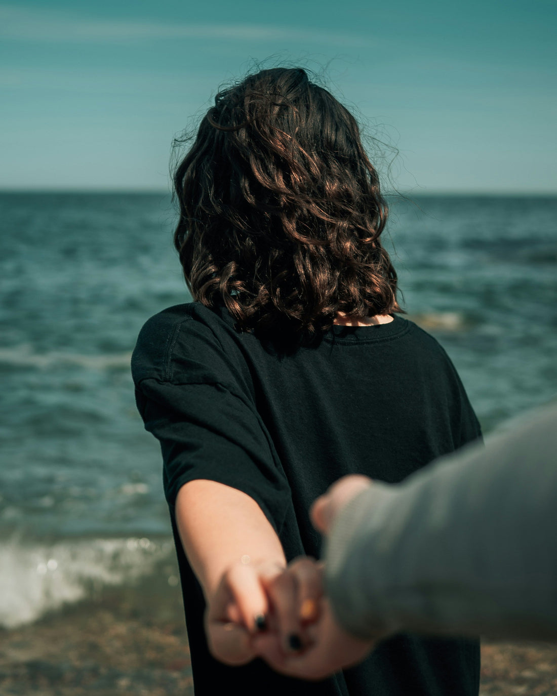 Woman holding partners hand behind her facing the sea