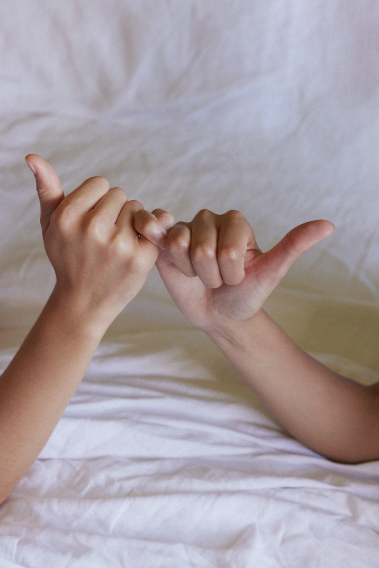 Two women's hands holding each other on a white bedspread