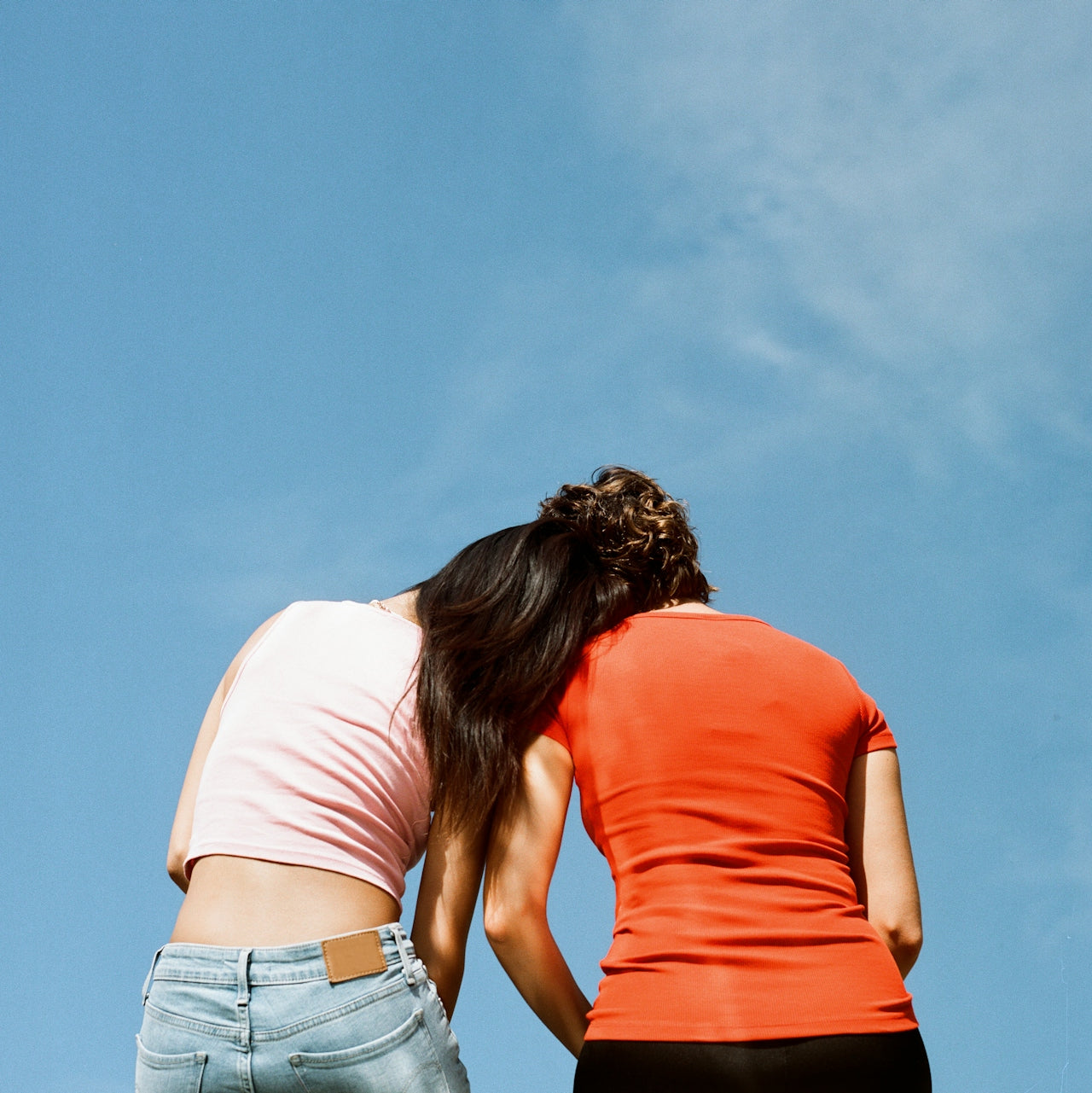 Two women standing back-to-back against a clear blue sky