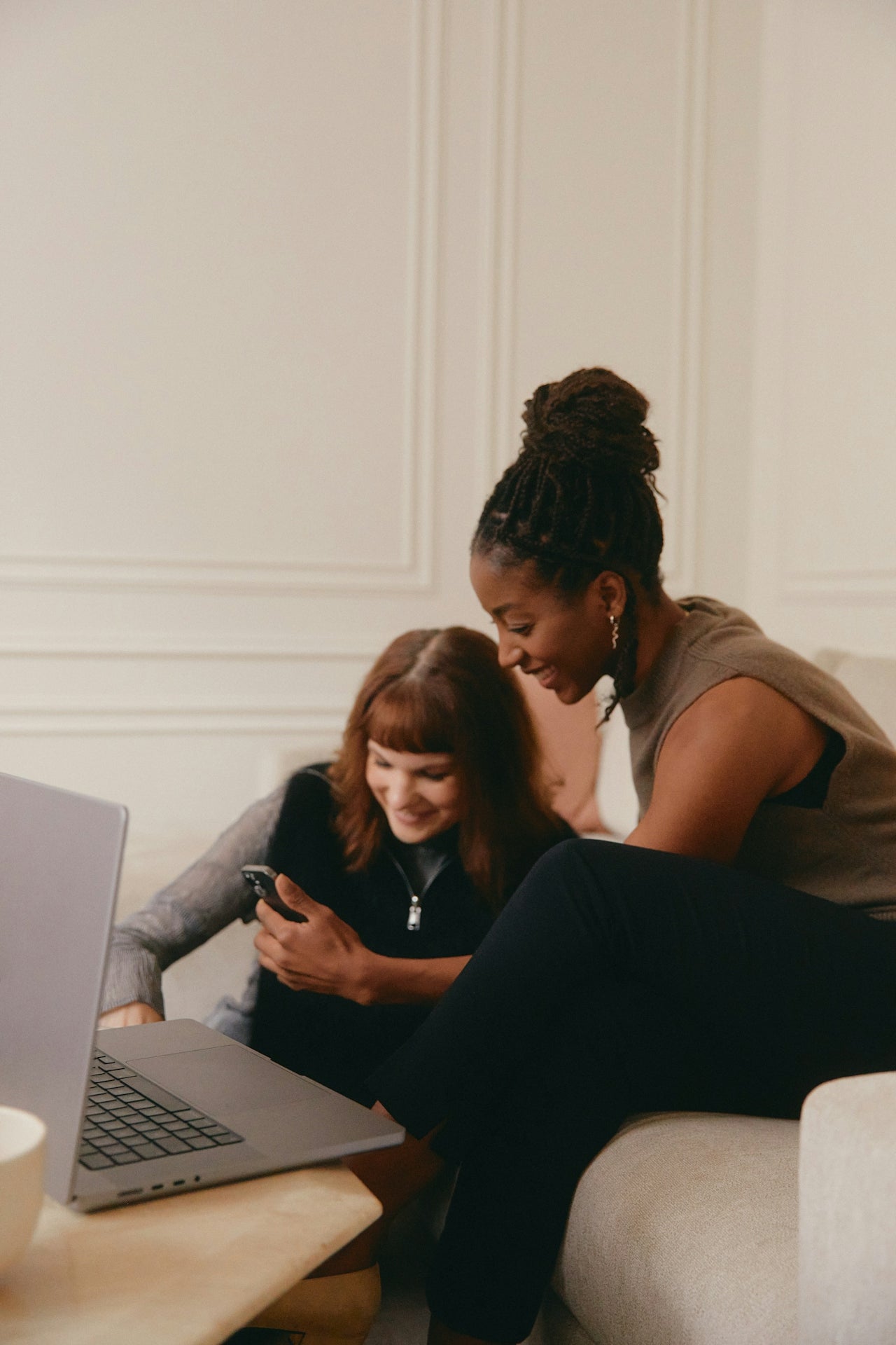 Two women sitting on a couch looking at a laptop together.
